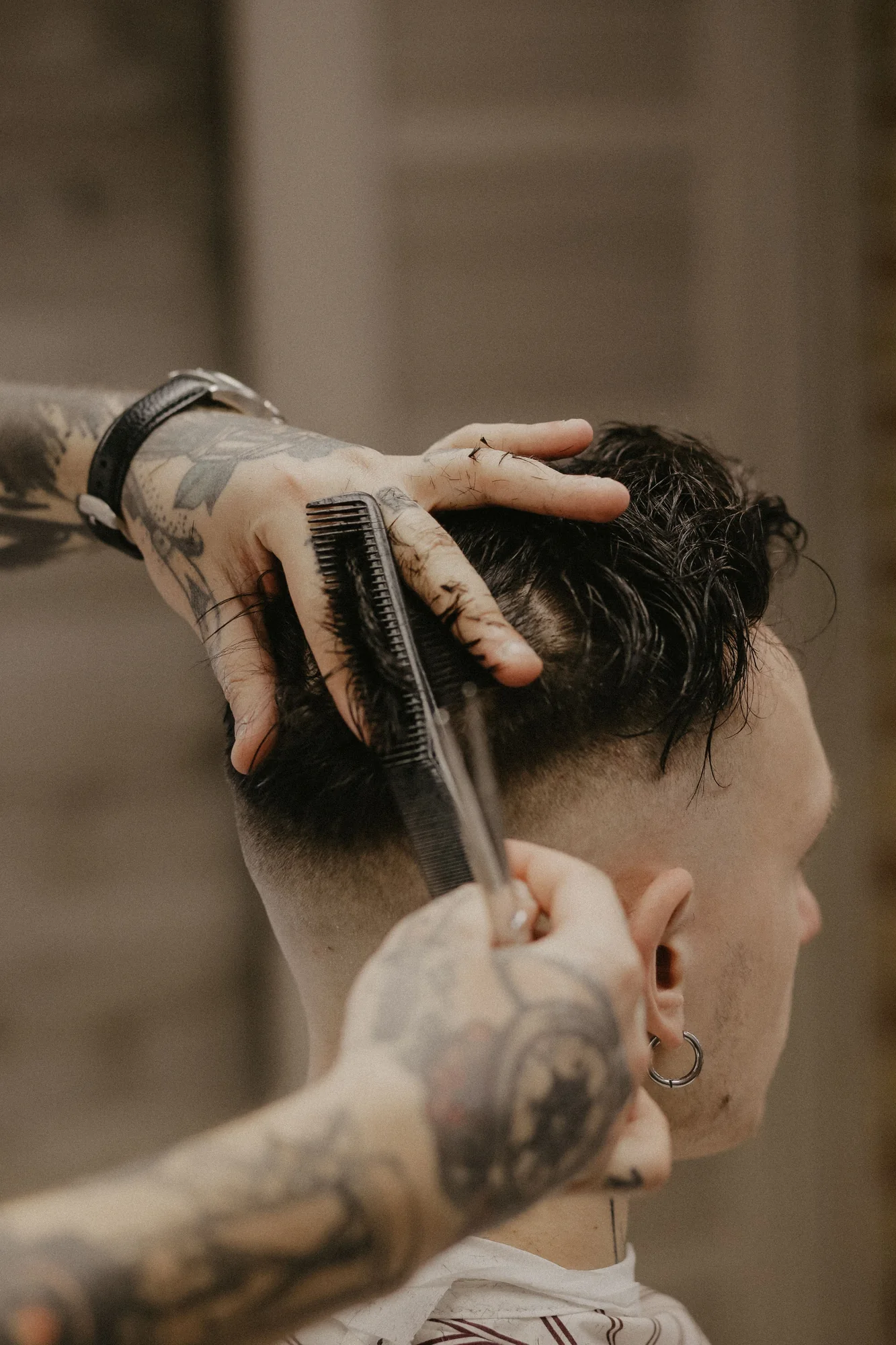 Close-up demonstration image of a barber combing and cutting dark hair over a taper.