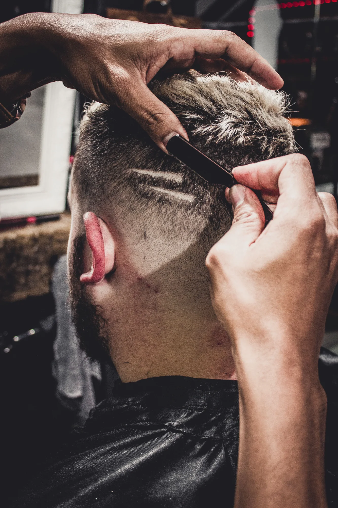Close-up demonstration image of a barber refining a fade at the hairline with a razor.